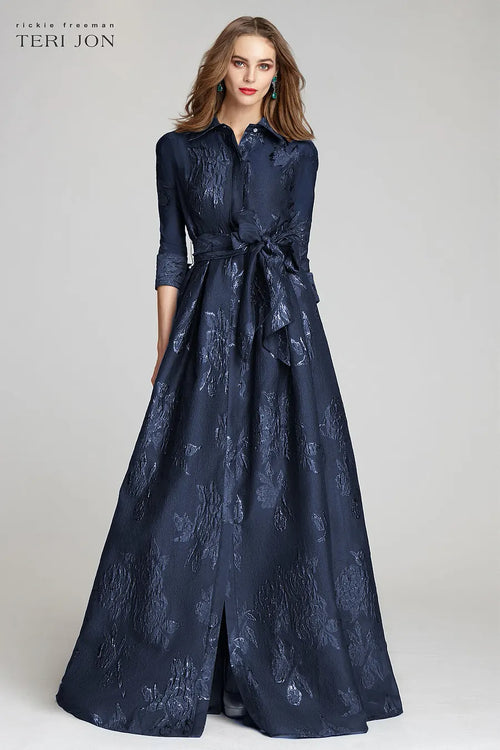 Model wearing Teri Jon 207015 floral shirt gown with a collared neckline, sash belt, three-quarter sleeves, and full A-line skirt.