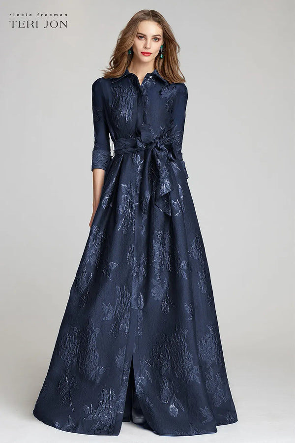 Model wearing Teri Jon 207015 floral shirt gown with a collared neckline, sash belt, three-quarter sleeves, and full A-line skirt.