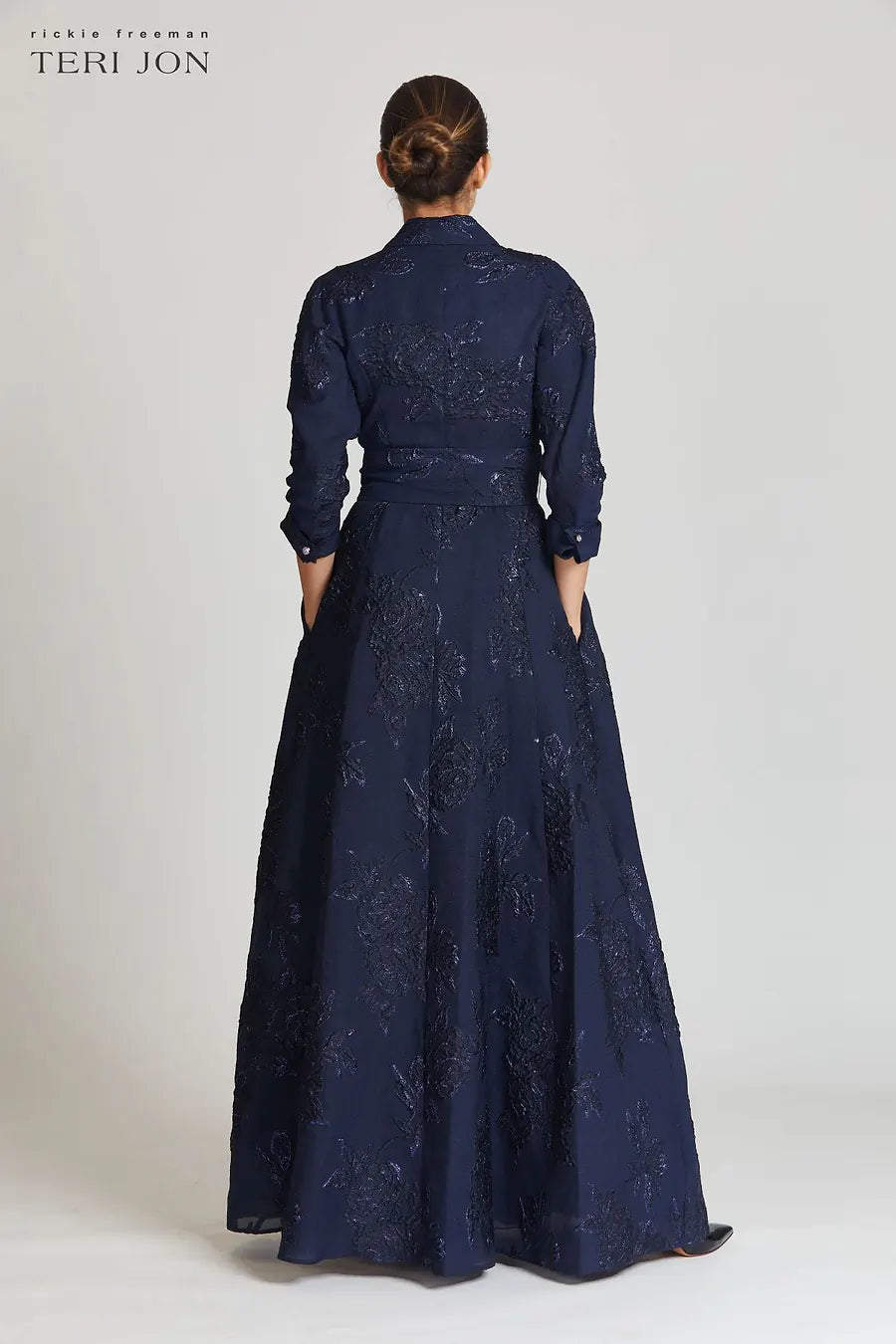 Model wearing Teri Jon 207015 floral shirt gown with a collared neckline, sash belt, three-quarter sleeves, and full A-line skirt.