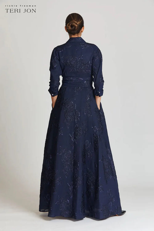 Model wearing Teri Jon 207015 floral shirt gown with a collared neckline, sash belt, three-quarter sleeves, and full A-line skirt.