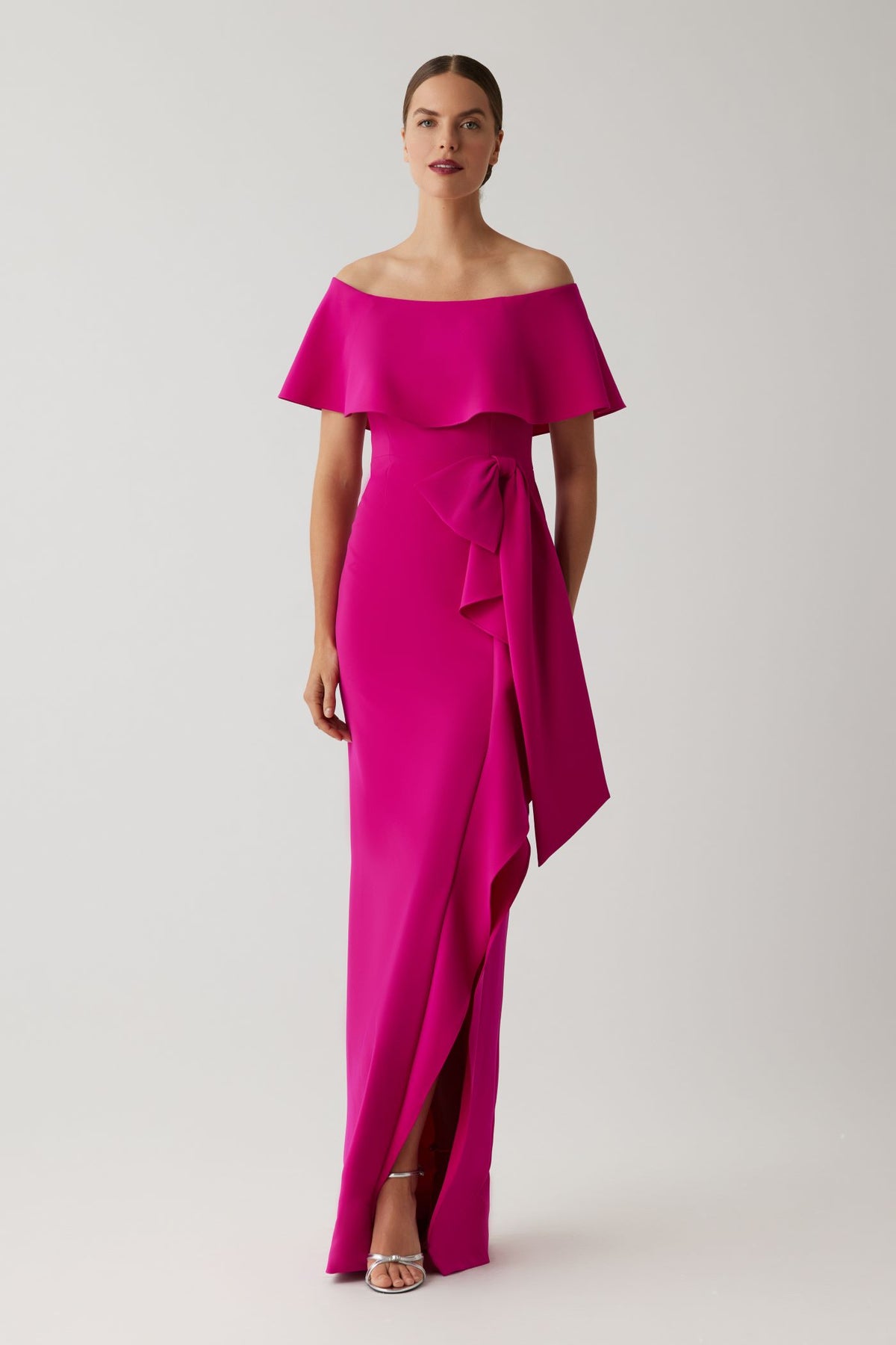 Model wearing Teri Jon 267000 off-shoulder evening gown featuring a flounce neckline, waist bow detail, fitted silhouette, and front slit.