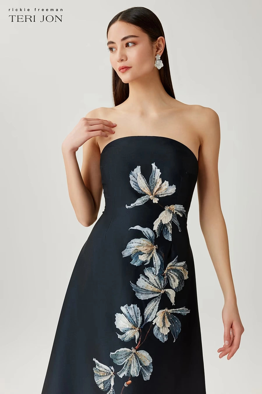 Woman wearing a black strapless dress with floral embroidery on a light gray background