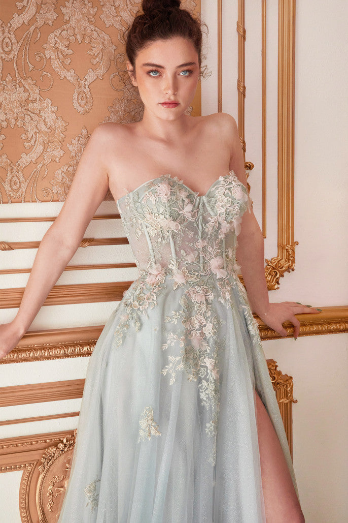 Strapless ball gown by Andrea & Leo, style A1089. Features intricate and delicate details with sheer floral appliqué corset bodice, leg slit, and over skirt. Available in Sage, Paris-Blue, and Blush-Mauve colors.